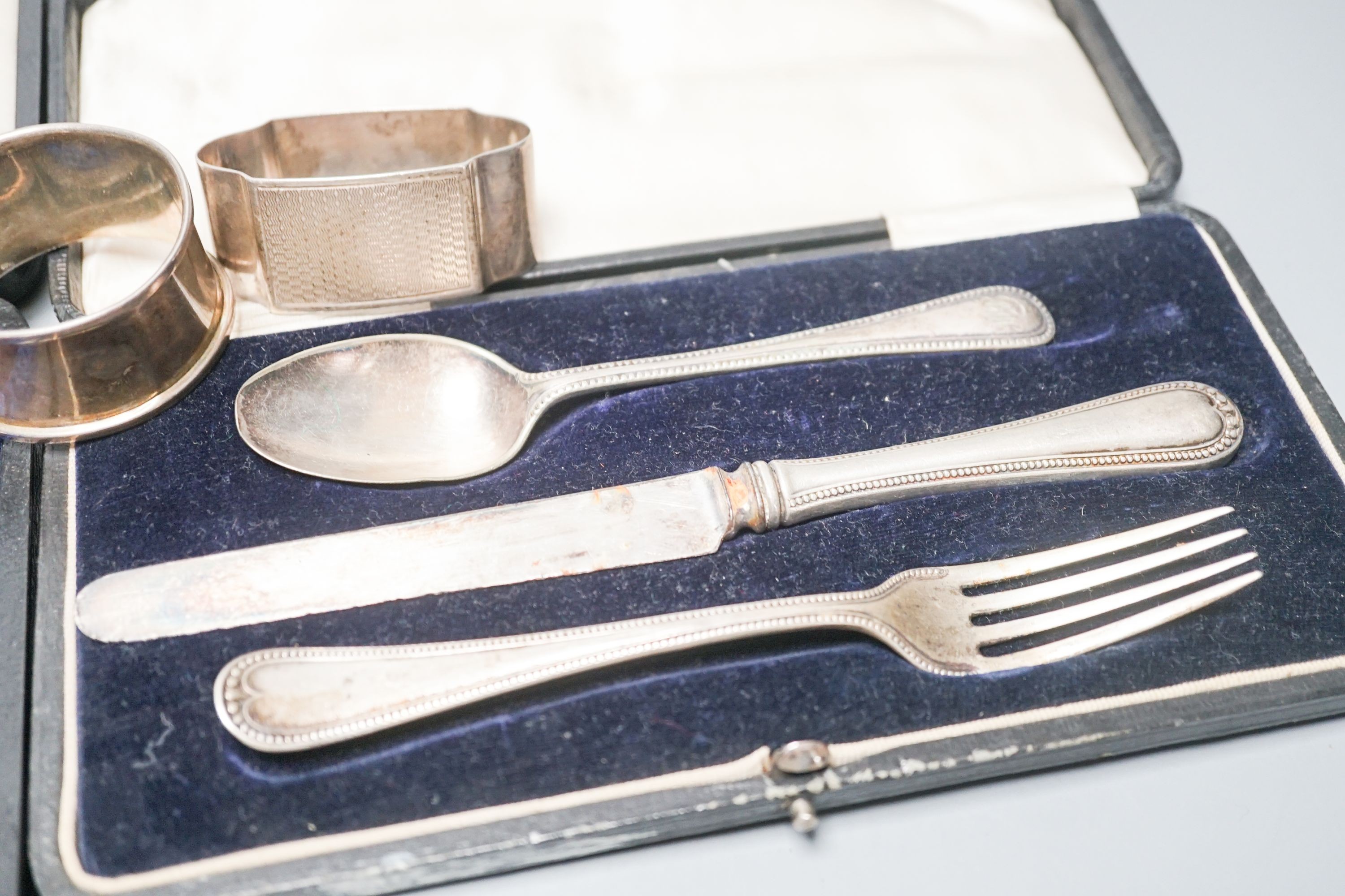 A cased set of six silver teaspoons, a cased christening set, three silver napkin rings and a silver dwarf candlestick.